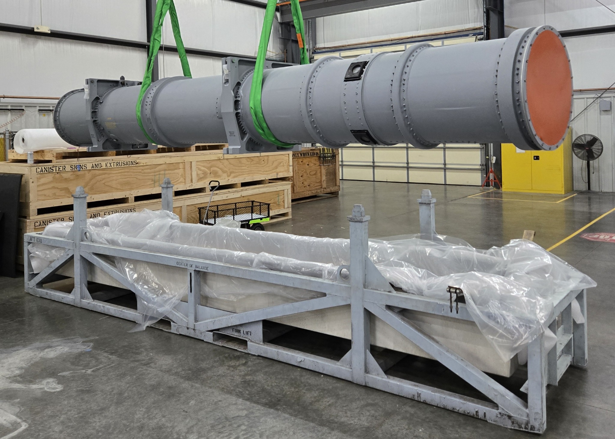 Large aerospace assembly lifted by an overhead crane inside the D-J Engineering manufacturing facility